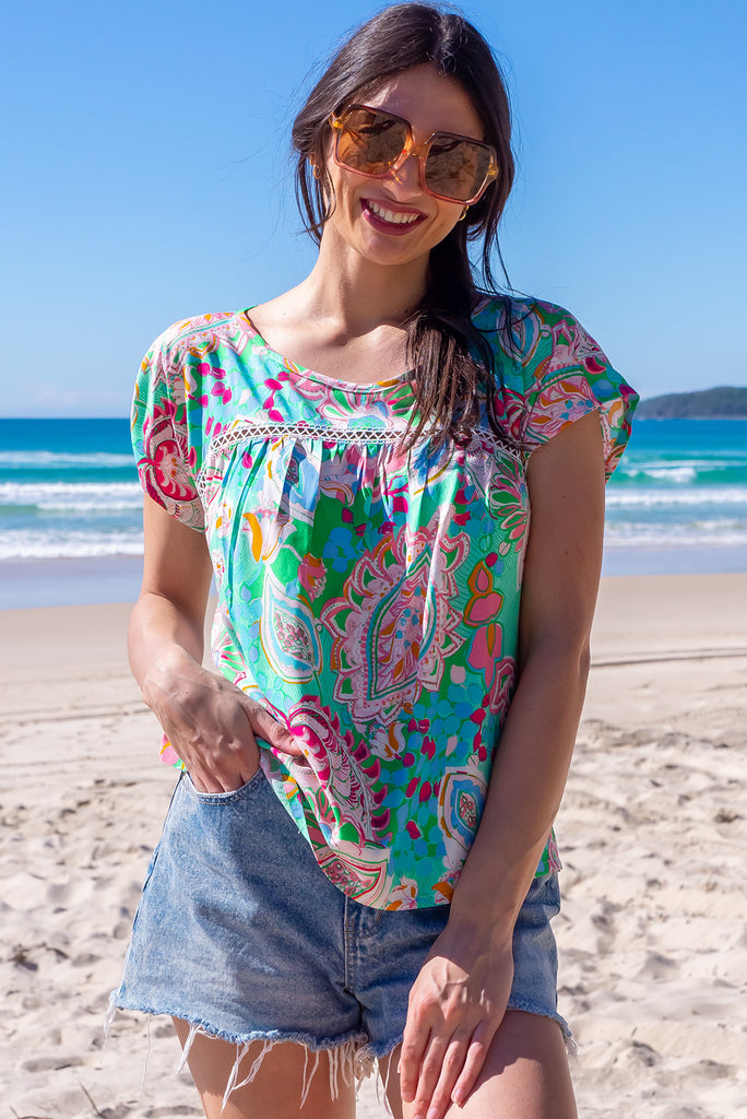 The Day Tripper Green Leaf Top is a gorgeous green t-shirt with a large, abstract leaf print. The top features a scooped neckline, lace insert across the chest, cap sleeves, and a amall split in the side seams. Made from woven rayon.