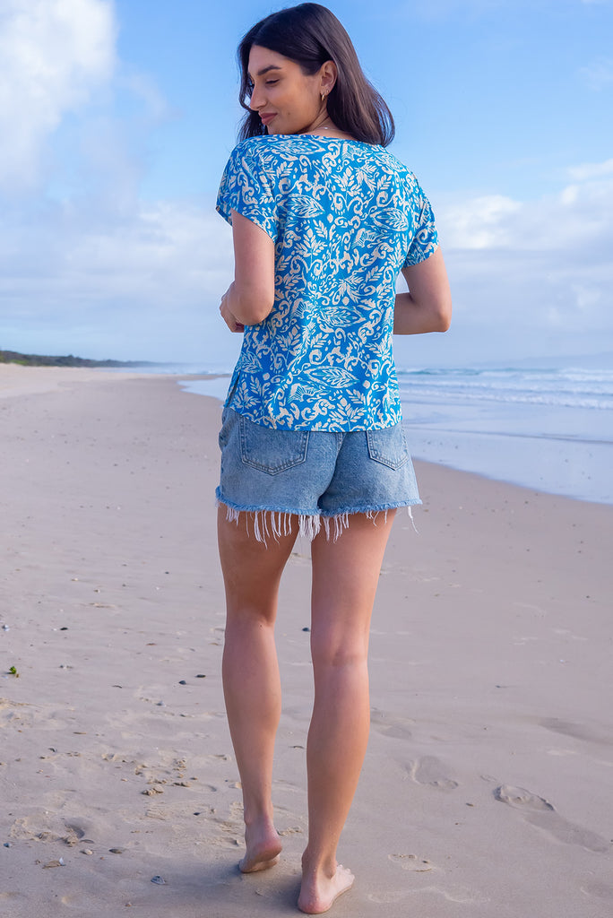 The Day Tripper Top Blue Atoll is a beautiful blue based shirt with a cream paisley print. The top features a scooped neckline, lace insert across the chest, cap sleeves, and a small split in the side seams. Made from woven rayon.