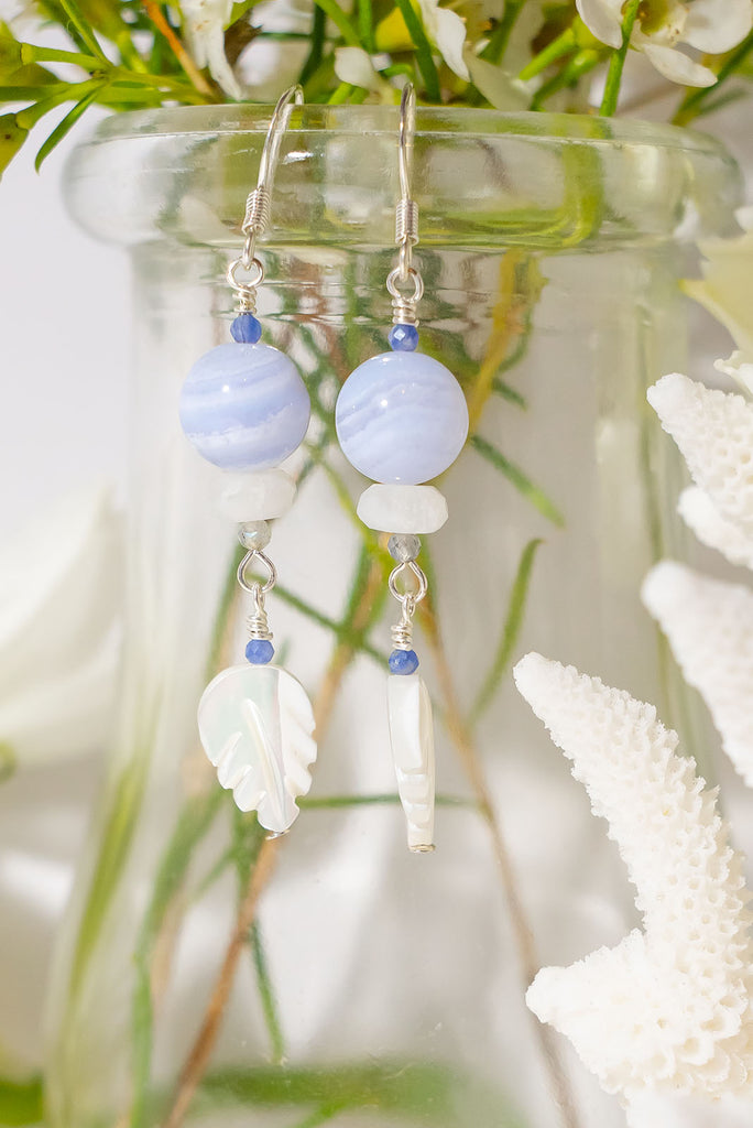 The Earrings Silver Droplet Blue Lace Agate are a beautiful pair of handmade earrings features natural gemstones including kyanite, moonstone, blue lace agate, and carved mother of pearl.