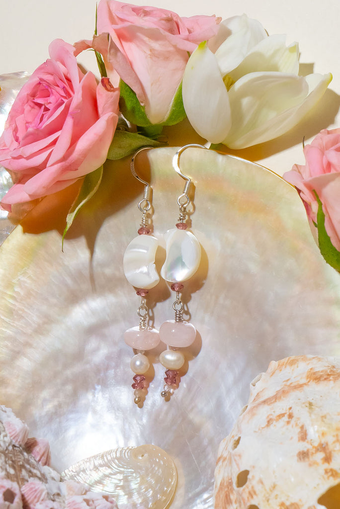 The Earrings Silver Droplet Shell Moon are a gorgeous pair of handmade earrings. The earrings feature natural gemstones including rhodolite garnet, mother of pearl, rose quartz, moonstone, and cultured pearls.