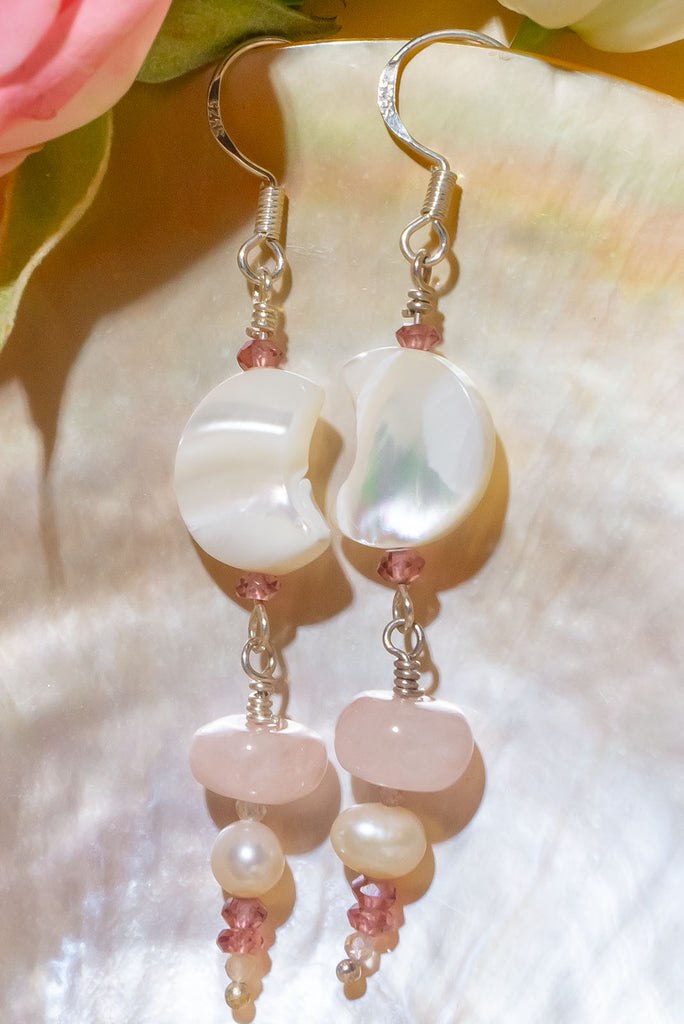 The Earrings Silver Droplet Shell Moon are a gorgeous pair of handmade earrings. The earrings feature natural gemstones including rhodolite garnet, mother of pearl, rose quartz, moonstone, and cultured pearls.