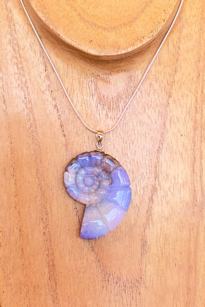 An Australian solid boulder opal pendant in the shape of a Nautilus sea shell, it has deep crystalline detail in mauve, purple and blue with slight flashes of pink. The back of the heart is polished boulder stone.