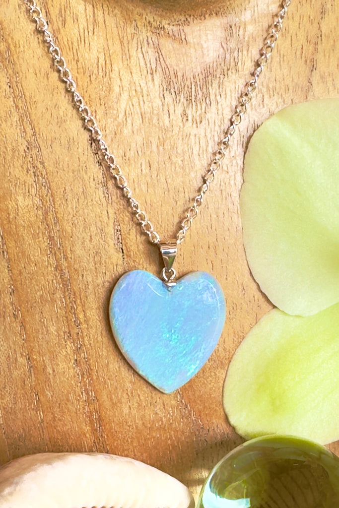 An Australian solid boulder opal pendant in a heart shape, misty mauve with very bright flashes of bright green and blue streaking across the whole stone.. This stone shows different colouration from different angles and is stunning in the sunlight.