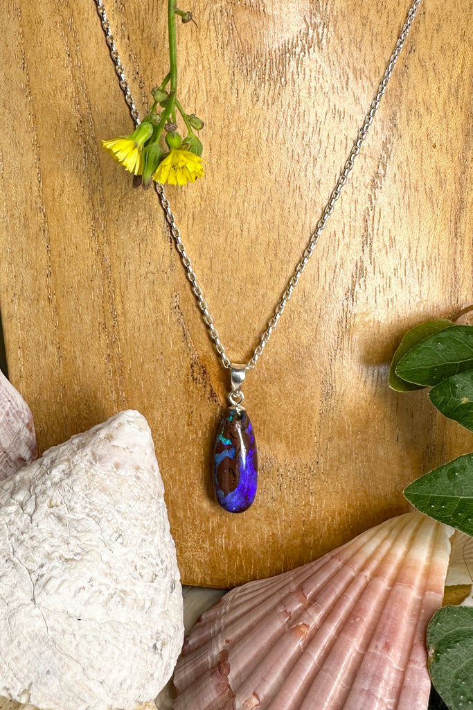 elegant droplet shaped opal pendant, with wonder pools of deep blue purple crystal, with a landscape of dark islands through