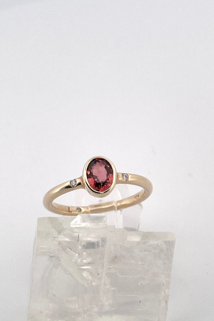 A beautiful simple ring designed to complement the lovely deep peachy red tourmaline gemstone set into the ring. The shank of the ring has a diamond on each side of the centre stone. 