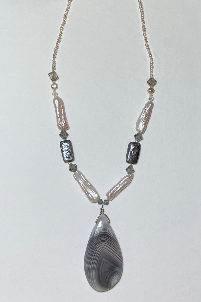 The centre piece is a wonderful misty grey and white banded Agate cut in a freeform droplet shape that enhances the curves of the stone. The necklace is made with four lovely pale pink pearls, two irredescent grey pearls, smoky quartz beads and swarovski crystal beads. 