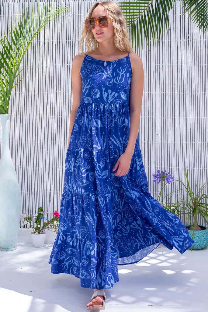 The Lulu Darling Ocean Deep Maxi Dress is a beautiful blue maxi dress with a pale blue seashell print. The dress features a high neckline, tiered skirting and side pockets, Made from a woven blend of cotton and rayon.
