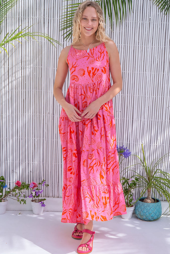 The Lulu Darling Sea Life Pink Maxi Dress features a high neck with thin straps, high cut under arms, full tiered skirting from the bust down and deep side pockets. The pink based dress has a large, red sea shell print all over. White spots may appear in the print due to the texture of the fabric. Made from 100% cotton.
