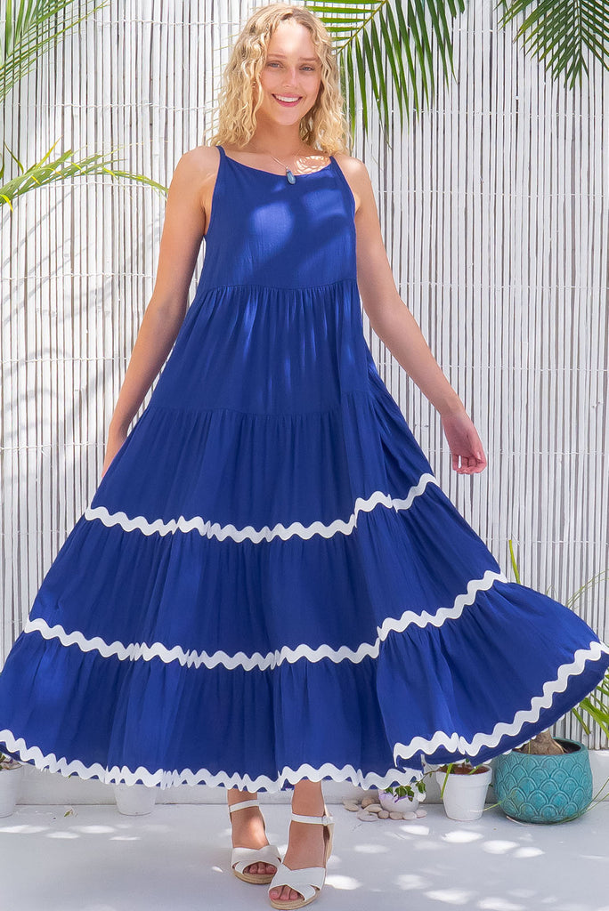 The Lulu Ric Rac Cobalt Maxi Dress is a beautiful blue maxi dress with a white oversized ric-rac braid feature. The maxi dress features a high neck, high cut under the arms, full tiered skirt falling from under bust, ric-rac on bottom three tiers, side pockets, and is made from woven cotton. 
