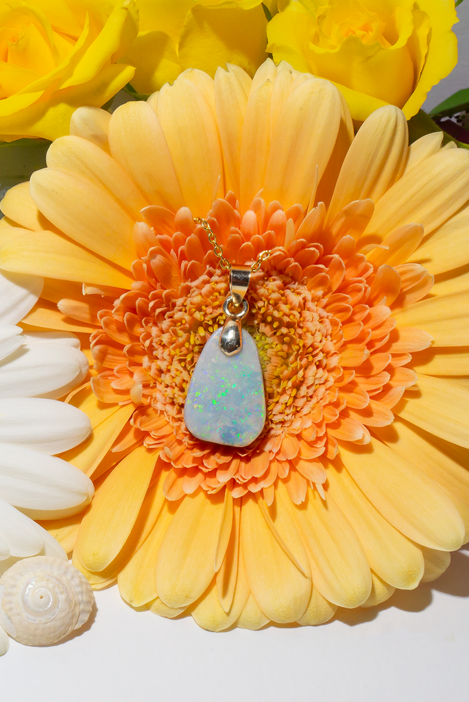 An opal pendant cut and polished into a softly curved freeform triangle, using Australian boulder opal. This is a very softly coloured piece with pale misty mauve pink base, shot through with sparkling flecks of very bright green.