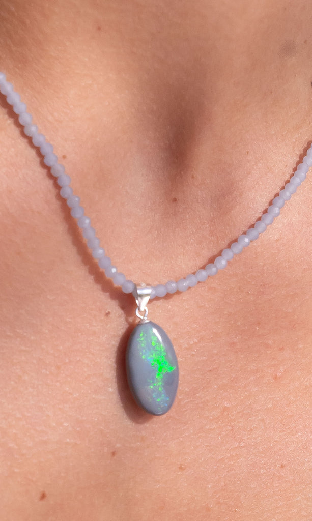 This intriguing and unique piece of Australian Crystal Opal has a grey base and bright green, yellow and some red flashes. This mystical pendants surface has a beautiful polish.