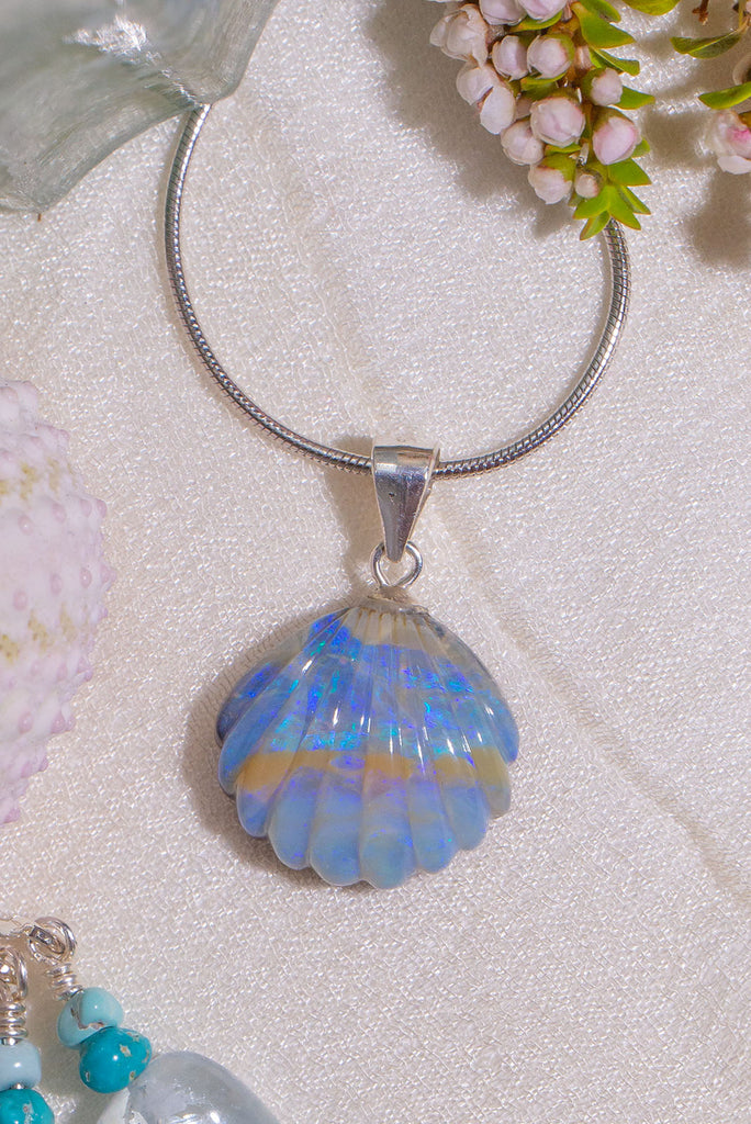 A tiny and really beautiful Australian boulder opal pendant, it is carved into in the shape of a scallop shell, it has a bright misty purplish blue crystalline surface.