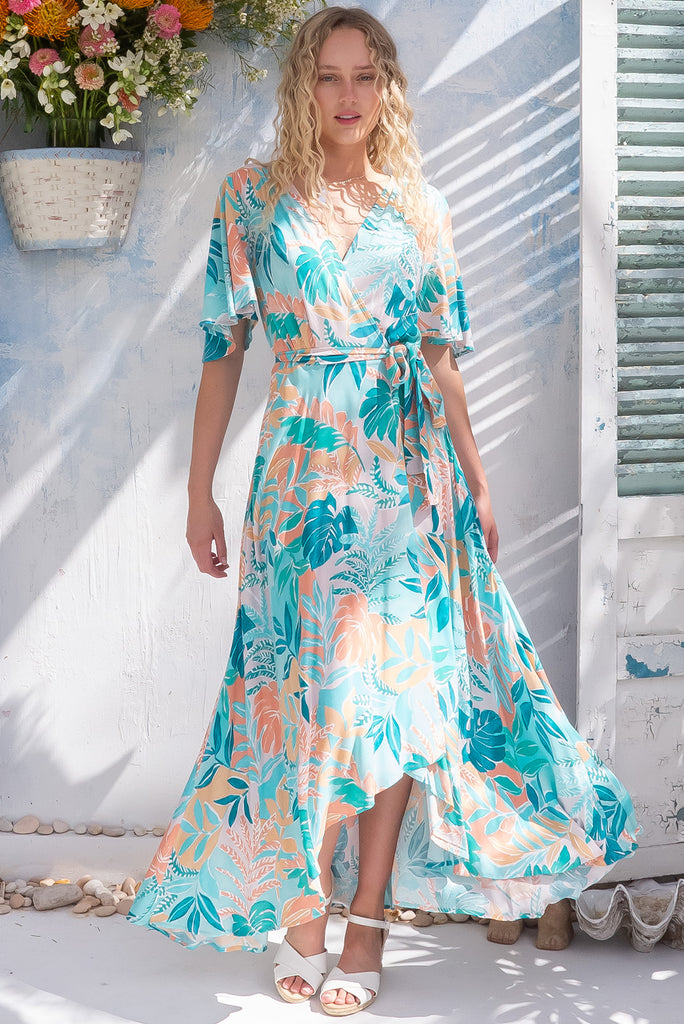 The Petal Island Wave Maxi Wrap Dress is a beautiful pale blue wrap dress with a pastel hued, large, tropical leaf print. The dress features flutter sleeves, a functional wrap design, and side pockets. Made from 100% rayon.
