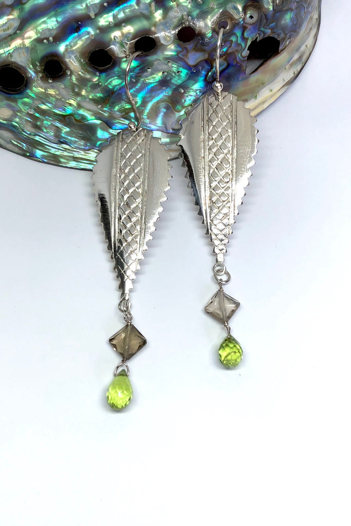 The African inspired design of these earrings was obtained by casting a pair of Mozambique Ebony wood earrings in silver. A Peridot gemstone briolet and a faceted smoky quartz hang from the base. 
