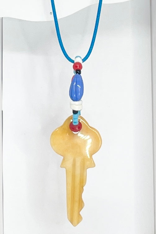 A key made of stone which hangs from a circlet of simple bright village beads. Then suspended from a blue cotton necklace.