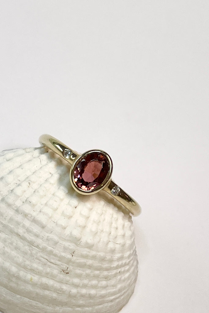 A beautiful simple ring designed to complement the lovely deep peachy red tourmaline gemstone set into the ring. The shank of the ring has a diamond on each side of the centre stone. 