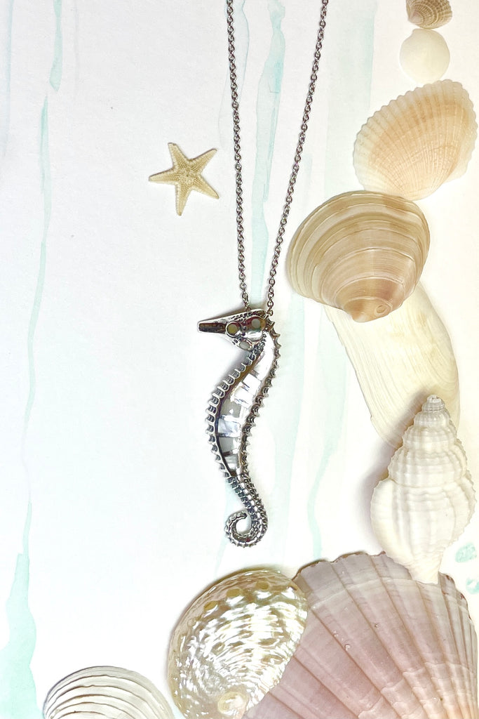 A silver seahorse on a silver chain which has been inlaid with mother of pearl shell,