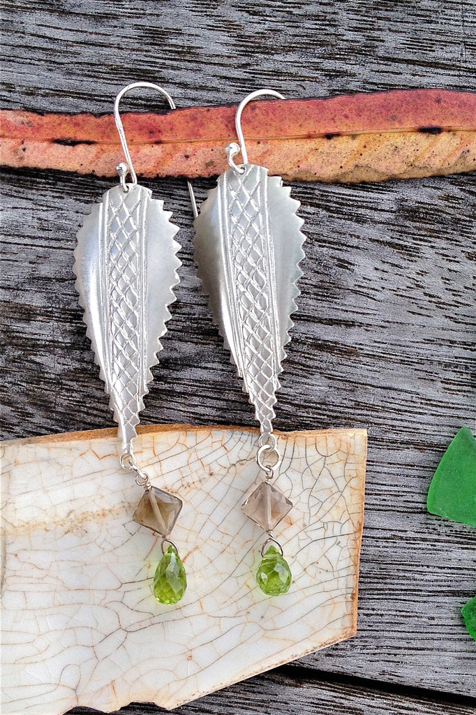 The African inspired design of these earrings was obtained by casting a pair of Mozambique Ebony wood earrings in silver. A Peridot gemstone briolet and a faceted smoky quartz hang from the base. 