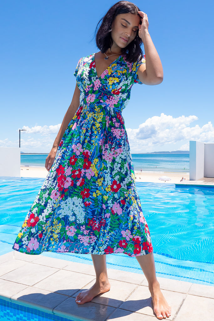 This Style Features A Deep V Neckline, Fitted Basque Waist With Gathered Bust, Side Pockets, Cap Sleeves And Elasticated Back For Maximum Comfort. The Monet Print  Is A Navy Base Adorned With Pin, Red, Yellow, Blue, Green And White Medium Sized Florals. Made From 100% Cotton