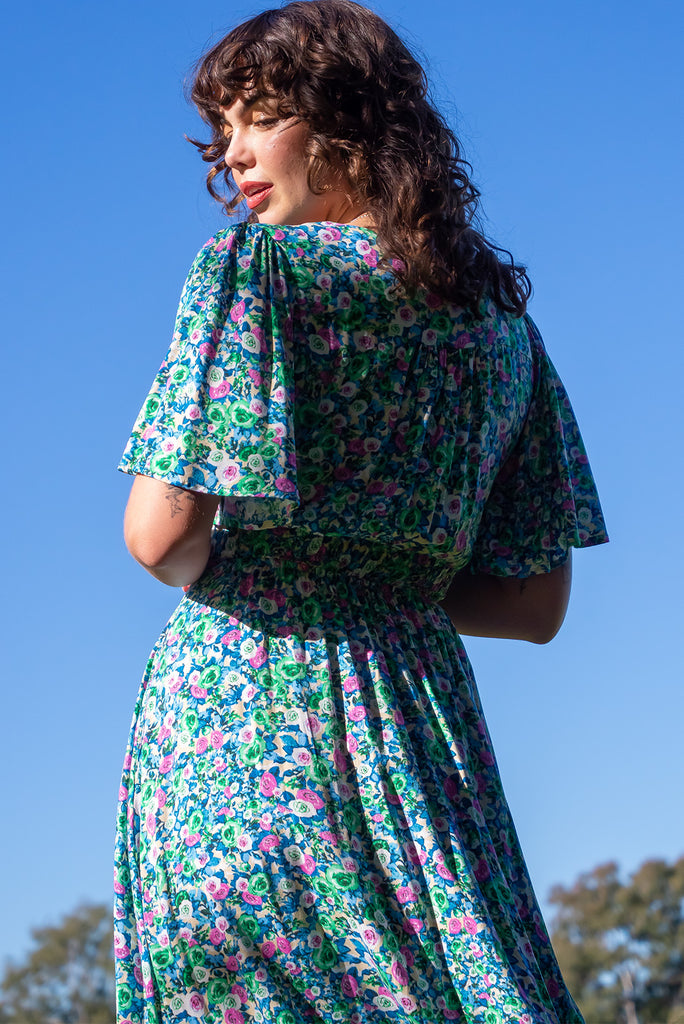 The Annie Tinker Blue Midi Dress is beautiful blue dress with a floral print in blues, greens and pink. The dress features flutter sleeves, a deep v neckline, fitted basque waist with gathered bust, elastic shirring at back waist, side pockets and is made from woven 100% rayon.