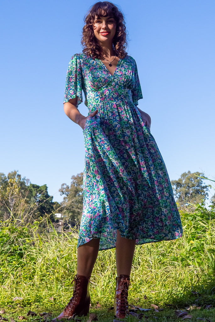 The Annie Tinker Blue Midi Dress is beautiful blue dress with a floral print in blues, greens and pink. The dress features flutter sleeves, a deep v neckline, fitted basque waist with gathered bust, elastic shirring at back waist, side pockets and is made from woven 100% rayon.