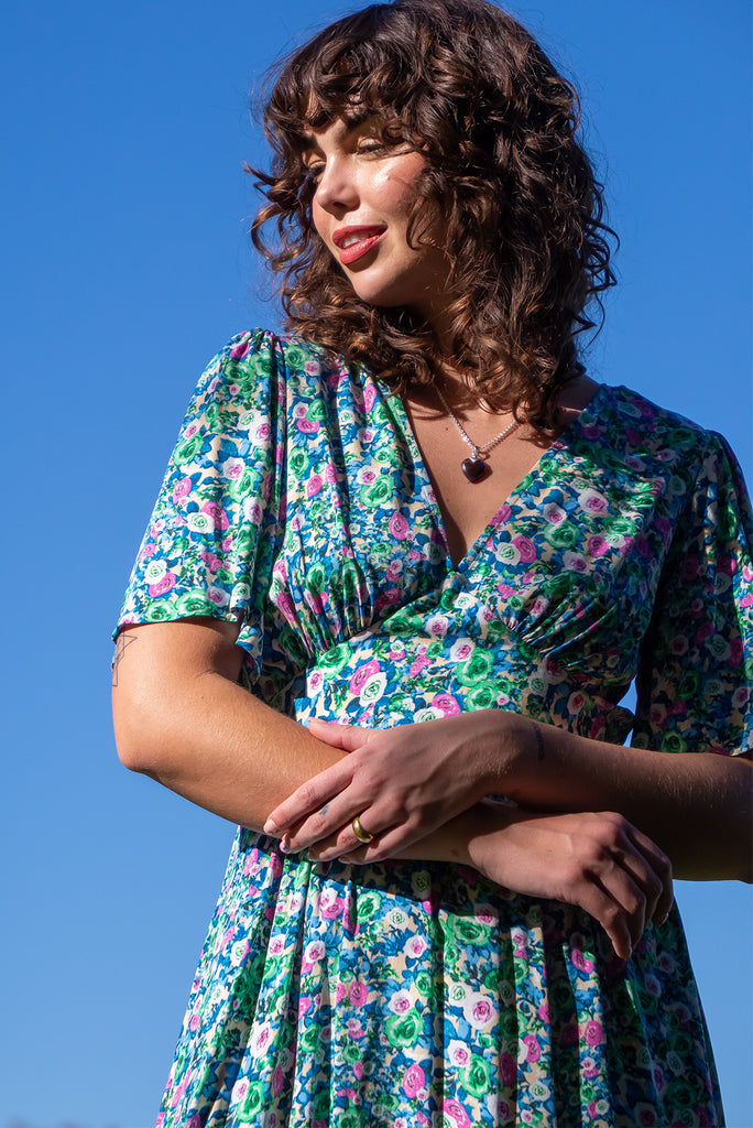 The Annie Tinker Blue Midi Dress is beautiful blue dress with a floral print in blues, greens and pink. The dress features flutter sleeves, a deep v neckline, fitted basque waist with gathered bust, elastic shirring at back waist, side pockets and is made from woven 100% rayon.