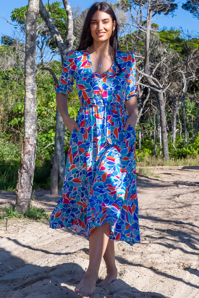 The Camellia Athens Blue Midi Dress is a beautiful blue midi dress with a multicoloured floral mosaic style print. The dress features functional buttons from front chest to waist, adjustable drawstring at either side of waist, frill v-neckline, 3/4 sleeves, and side pockets. Made from woven rayon.