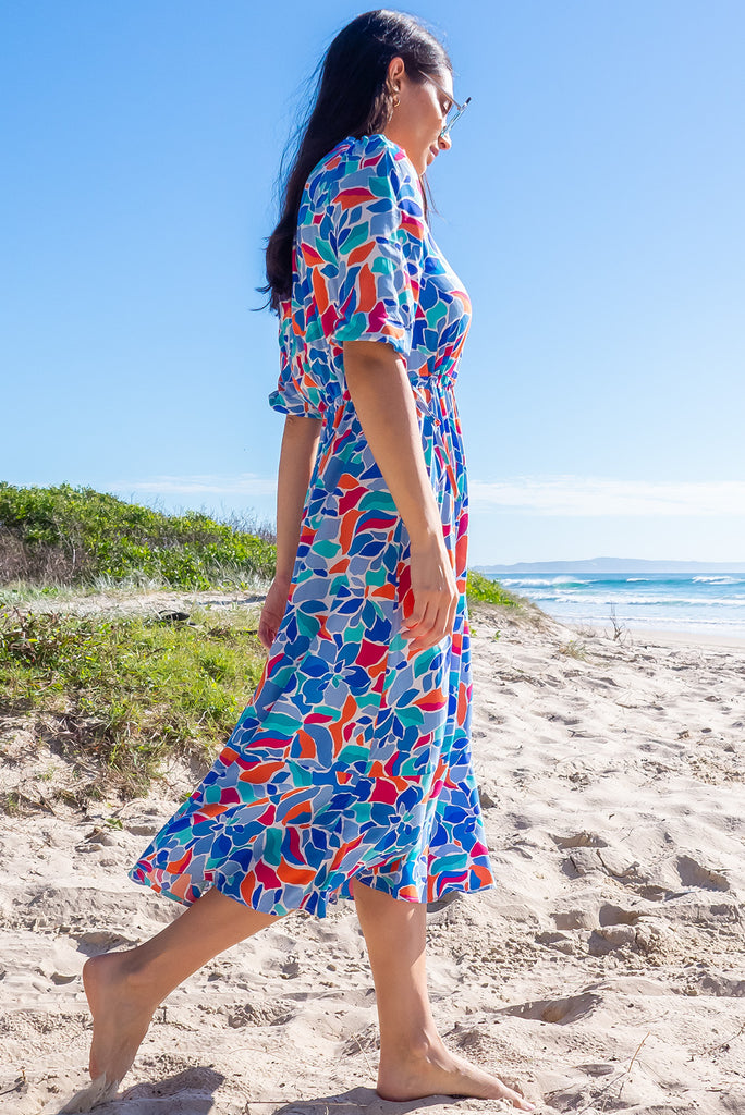The Camellia Athens Blue Midi Dress is a beautiful blue midi dress with a multicoloured floral mosaic style print. The dress features functional buttons from front chest to waist, adjustable drawstring at either side of waist, frill v-neckline, 3/4 sleeves, and side pockets. Made from woven rayon.