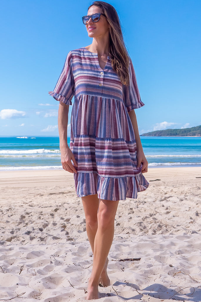 The Charlise Amethyst Stripe Mini Dress is a navy, marron and white striped mini dress. The dress features short sleeves with frill detailing on the cuff, a split neckline with function button down chest to waistline, tiered skirting from the waist down, and side pockets. Made from woven cotton and polyester.