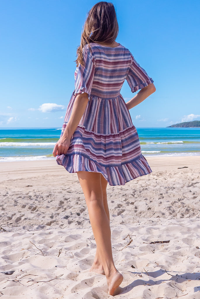 The Charlise Amethyst Stripe Mini Dress is a navy, marron and white striped mini dress. The dress features short sleeves with frill detailing on the cuff, a split neckline with function button down chest to waistline, tiered skirting from the waist down, and side pockets. Made from woven cotton and polyester.