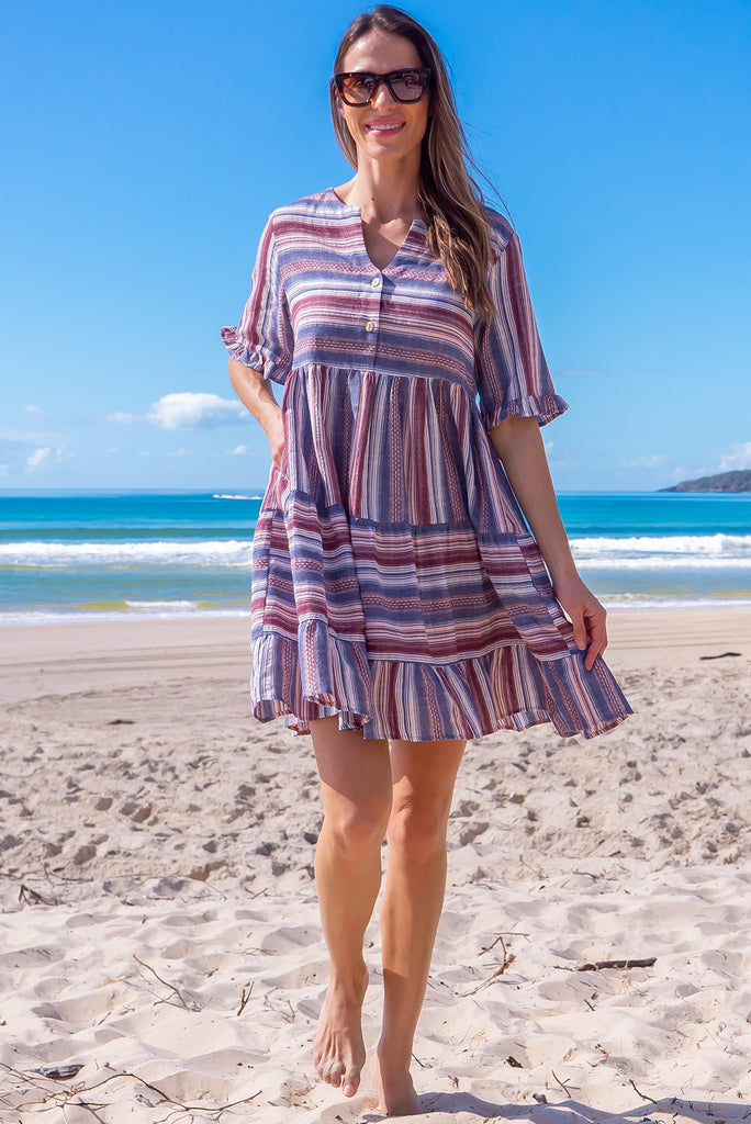 The Charlise Amethyst Stripe Mini Dress is a navy, marron and white striped mini dress. The dress features short sleeves with frill detailing on the cuff, a split neckline with function button down chest to waistline, tiered skirting from the waist down, and side pockets. Made from woven cotton and polyester.
