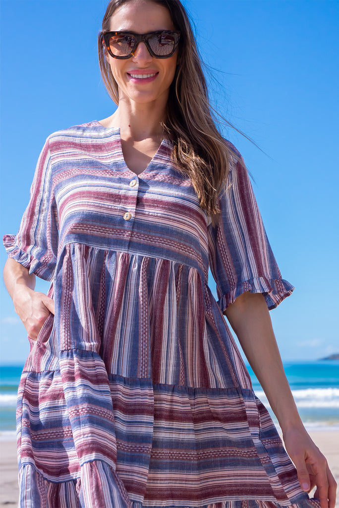 The Charlise Amethyst Stripe Mini Dress is a navy, marron and white striped mini dress. The dress features short sleeves with frill detailing on the cuff, a split neckline with function button down chest to waistline, tiered skirting from the waist down, and side pockets. Made from woven cotton and polyester.
