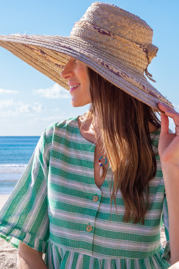 The Charlise Green Leaf Stripe Mini Dress is a green and white striped mini dress. The dress features short sleeves with frill detailing on the cuff, a split neckline with function button down chest to waistline, tiered skirting from the waist down, and side pockets. Made from woven cotton and polyester.