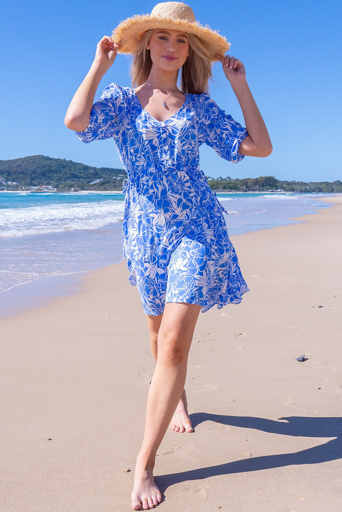 The Collette Blue Mono Mini Dress is a beautiful sky blue based mini dress with a with floral silhouette print. The dress features functional buttons from front chest to waist, adjustable drawstring at either side of waist, v-neckline, 3/4 sleeves, and side pockets. Made from woven rayon.