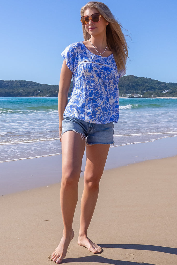 The Day Tripper Blue Mono Top is a beautiful sky blue based shirt with a with floral silhouette print. The top features a scooped neckline, lace insert across the chest, cap sleeves, and a small split in the side seams. Made from woven rayon.