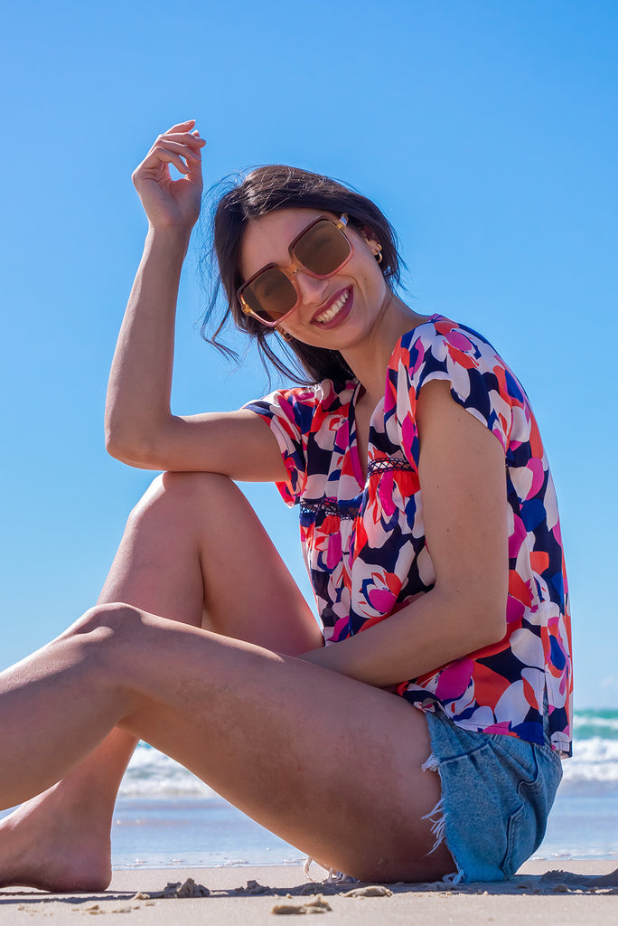 The Day Tripper Bold Summer Top is a gorgeous shirt with a bold floral print in pink, orange and blues. The top features a scooped neckline, lace insert across the chest, cap sleeves, and a small split in the side seams. Made from woven rayon.