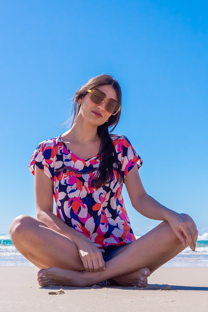 The Day Tripper Bold Summer Top is a gorgeous shirt with a bold floral print in pink, orange and blues. The top features a scooped neckline, lace insert across the chest, cap sleeves, and a small split in the side seams. Made from woven rayon.