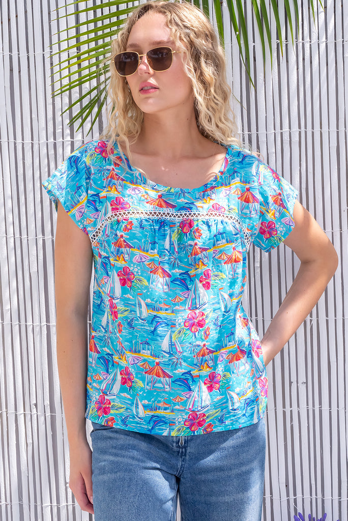 The Day Tripper In Paradise Top is a beautiful blue based blouse with a tropical floral and sailboat print. The blouse features a scoop neckline and lace insert across the chest. Made from 100% woven rayon.