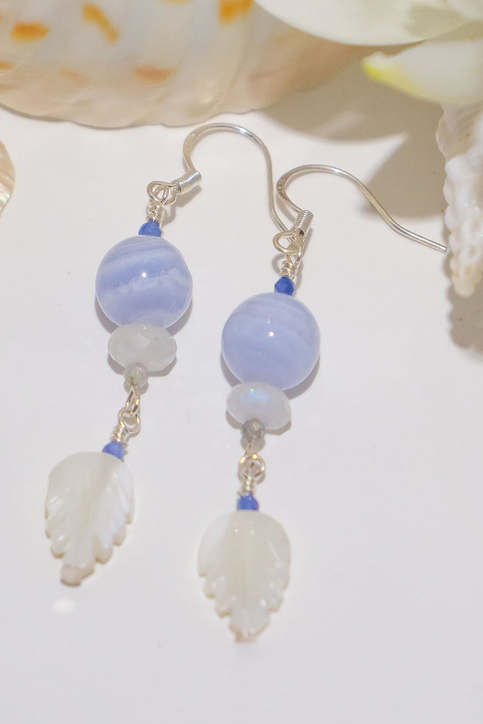 The Earrings Silver Droplet Blue Lace Agate are a beautiful pair of handmade earrings features natural gemstones including kyanite, moonstone, blue lace agate, and carved mother of pearl.