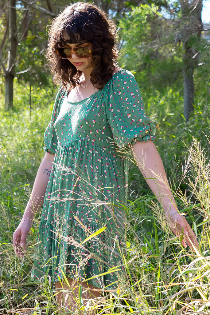 The Emelia Green Flowers Short Dress is a gorgeous green mini dress with a small white and pink floral print. The mini dress features 3/4 sleeves with elastic cuffs, tiered skirting and side pockets. Made from a woven blend of crinkle rayon.
