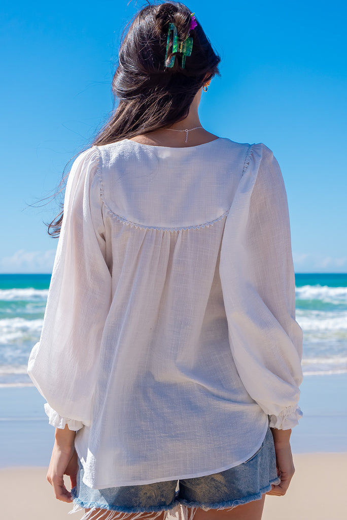 The Emmylu White Cotton Boho Blouse is a beautiful white blouse. The blouse features a yoke neckline with functional buttons, long flowy sleeves with elasticated cuffs, and a slightly longer back. Made from woven 100% cotton. 
