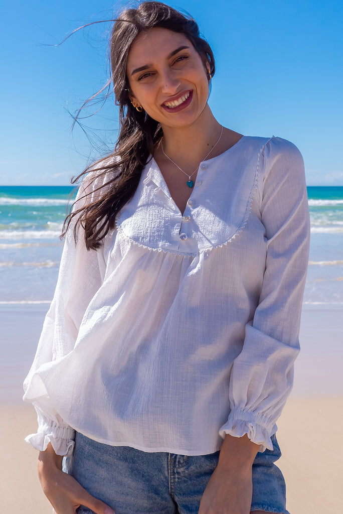 The Emmylu White Cotton Boho Blouse is a beautiful white blouse. The blouse features a yoke neckline with functional buttons, long flowy sleeves with elasticated cuffs, and a slightly longer back. Made from woven 100% cotton. 