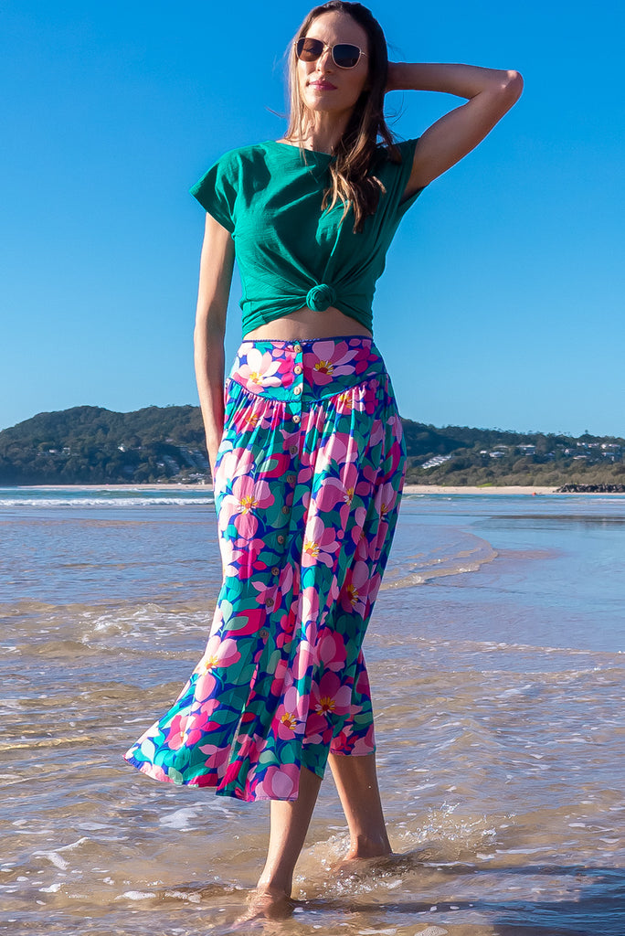 The Flirt Flora Button Front Maxi Skirt is a beautiful blue based skirt with a bright, pink and green floral print. The skirt features a waist yoke with blue piping, functional buttons from waist to hem, elasticated back of waist, and side pockets. Made from 100% rayon. 