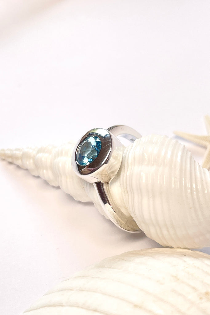 This chic ring has a modern twist to the design. The lovely round cut and faceted Aquamarine is set in a circle of polished 925 silver, perfectly setting off the blue. The bright blue stone is of excellent cut and clarity.