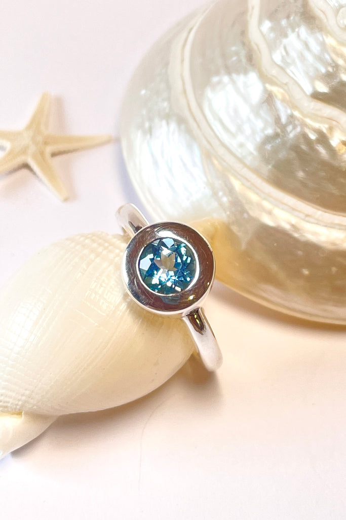 This chic ring has a modern twist to the design. The lovely round cut and faceted Aquamarine is set in a circle of polished 925 silver, perfectly setting off the blue. The bright blue stone is of excellent cut and clarity.