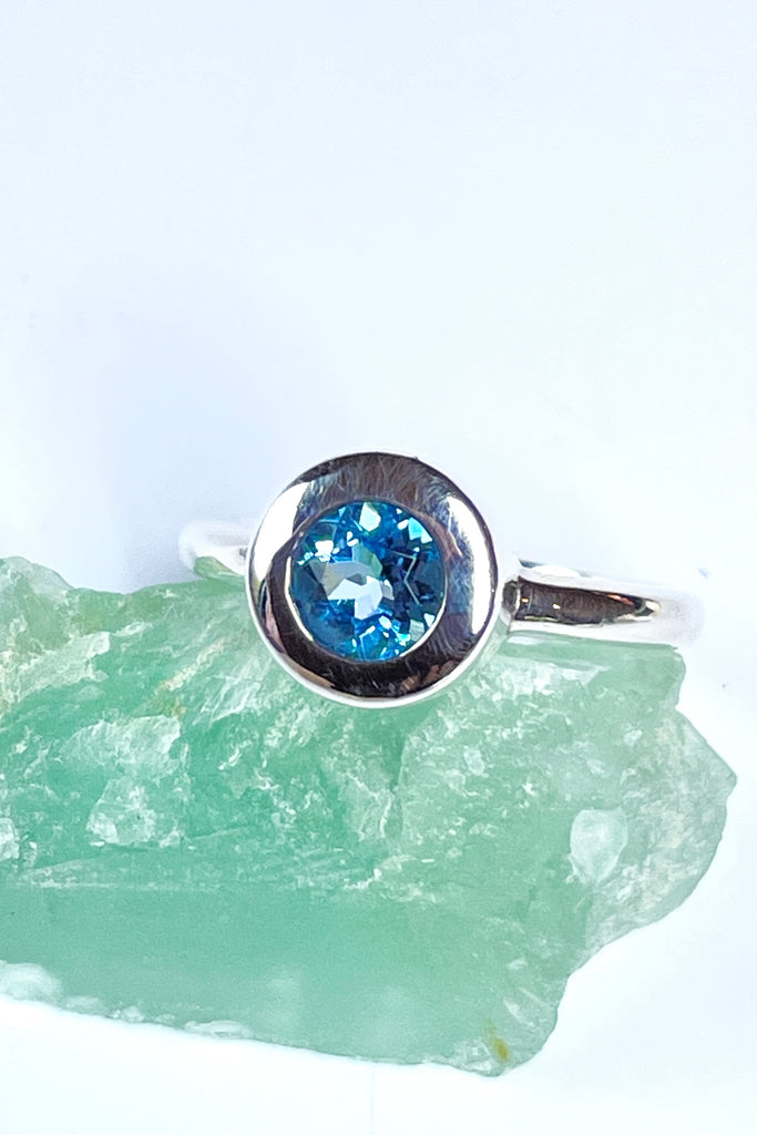 This chic ring has a modern twist to the design. The lovely round cut and faceted Aquamarine is set in a circle of polished 925 silver, perfectly setting off the blue. The bright blue stone is of excellent cut and clarity.