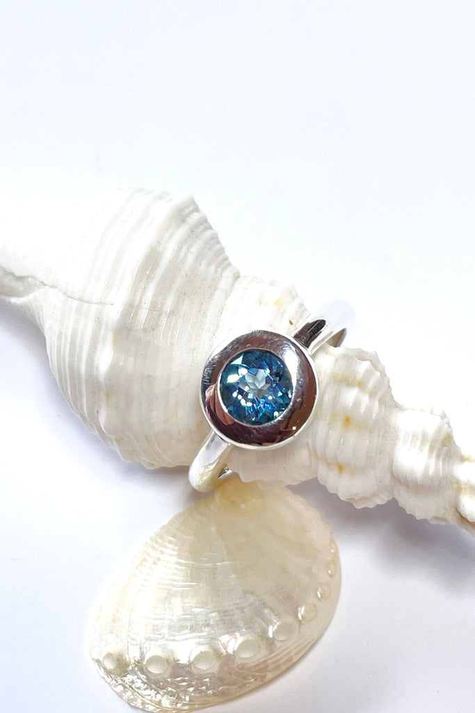 This chic ring has a modern twist to the design. The lovely round cut and faceted Aquamarine is set in a circle of polished 925 silver, perfectly setting off the blue. The bright blue stone is of excellent cut and clarity.