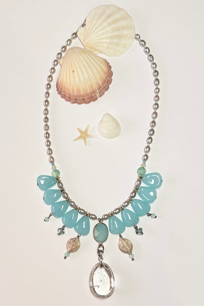 This pretty necklace is a one off piece made exclusively for Mombasa Rose Boutique, the hanging beads are aquamarine sea blue glass. The centrepiece is a gorgeous clear rutilated quartz. The necklace is of pale silvery grey natural pearls. This necklace is inspired by the ocean waves.