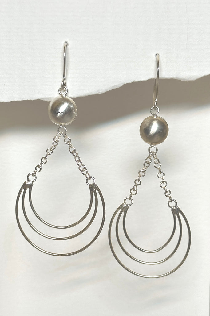 A lovely delicate handmade silver earring, the circle is a finely hammered dome. Suspended from the two chains swings a swoop of three tiny silver wires. The inspiration for this design was the wire work of Africa. 