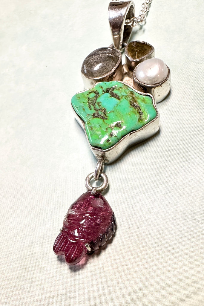 This intriguing pendant is an old piece, it has been handmade in Jaipur, India. It has a central stone of natural turquoise, the stones above are Labradorite, Citrine and natural pearl set in 925 silver. The hanging stone is a pink tourmaline carved into a fish and backed with silver.